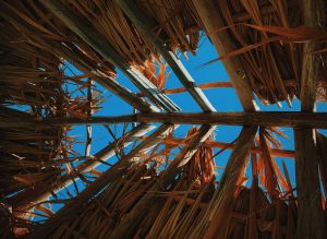 Wooden Roof Structure with sky visible through the beams. Structure is being covered with dried reeds.
