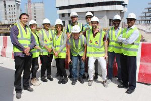 Group of people on construction site wearing white hard hats and fluorescent hi-vis jackets