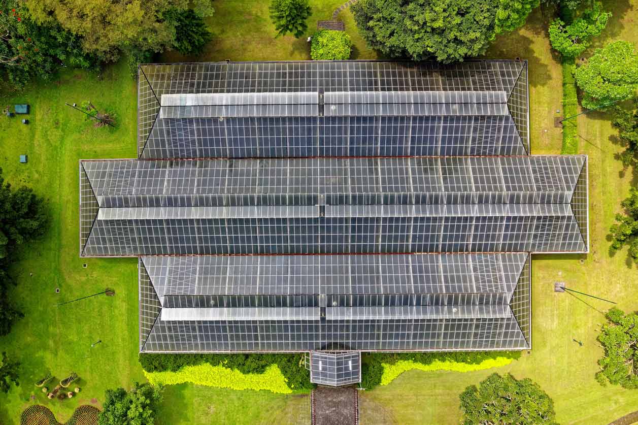 Aerial View of Solar Panel Roof. Building is surrounded by green grass and trees.