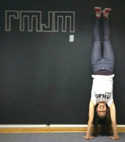 Brunette woman doing handstand against wall with chalk letters drawn on it.