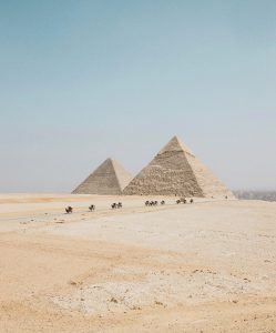 pyramids of giza in desert with travelling group and camels on dirt track